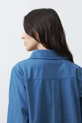 Camisa de manga larga en color azul oscuro con bordados florales en hilo blanco a lo largo de la botonadura frontal. Presenta cuello clásico y corte relajado.