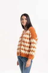 Cardigan de punto con diseño geométrico de rombos en colores naranja y crema. Presenta escote en V, cierre frontal con botones y puños y ruedo acanalados.