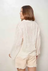 Camisa blanca de manga larga con bordados florales y detalles de ojales, cuello camisero y cierre frontal con botones ocultos.