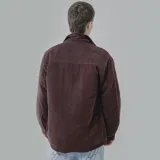 Campera color borgoña de pana con cuello camisero, cierre frontal con botones a presión y dos bolsillos de parche en el pecho. Interior acolchado con patrón de rombos.