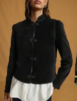 Chaqueta negra de estilo oriental con cuello alto estructurado y cierre frontal mediante nudos decorativos tradicionales. Presenta mangas largas con leve volumen en los hombros y un corte recto.