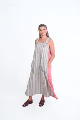 Vestido largo sin mangas de lino y algodón, con diseño a rayas verticales en tonos blanco y gris, y laterales en color rosado. Cuenta con breteles anchos con botones y bolsillos delanteros amplios.