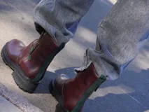 Botas de cuero marrón con suela track de goma negra, cierre lateral en color rojo y detalle de tira trasera al tono.