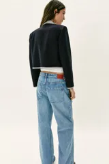 Blazer corta de color negro con cuello solapa, manga larga y hombreras. Presenta detalles combinados con estampado de cuadro vichy en el cuello, los bordes de la solapa, el ruedo y los puños. Cuenta con cierre frontal de un botón y falsos bolsillos delanteros de vivo.