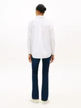 Camisa blanca de algodón orgánico con cuello camisero, cierre frontal de botones y manga larga ajustable con presilla. Cuenta con el logo de Tommy Hilfiger bordado sutilmente en el pecho.