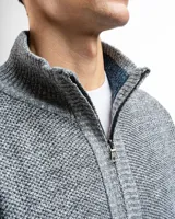 Campera de punto con cierre frontal, cuello alto y forro interno. Presenta un diseño de tejido jaspeado con puños y ruedo acanalados, e incluye un pequeño aplique de marca en la parte inferior.