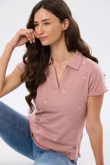 Remera polo de algodón color beige con mangas cortas, escote en V y cuello camisero. Presenta delicados mini bordados florales distribuidos en toda la prenda.