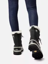 Bota de nieve Sorel modelo Caribou, con diseño impermeable de caña alta. Presenta una estructura de nubuck negro con costuras selladas, base de goma vulcanizada resistente al agua y forro interior de fieltro con borde de pelo sintético tipo Sherpa.