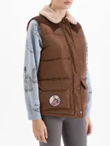 Chaleco matelaseado color marrón camel con canesú en corderoy color chocolate. Presenta cuello con corderito, cierre frontal con botones a presión, bolsillos con tapa y un parche bordado en el bolsillo derecho.