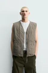 Chaleco acolchado de algodón color verde militar, de corte relaxed fit, con cuello en V, cierre frontal con cremallera y bolsillos de parche en la cadera. Presenta diseño acolchado con pespuntes ondulados y efecto lavado.