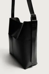 Bolso tipo shopper de diseño minimalista en color negro, con dos bolsillos planos exteriores y compartimento principal con cierre magnético. Incluye un bolsillo interior y asa de hombro ajustable.