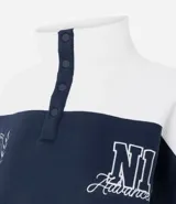 Buzo tipo polo de textura waffle con diseño color block en blanco y azul marino. Presenta cuello alto con cierre de botones, mangas largas y bordados decorativos en el frente.