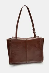Bolso tipo mini shopper confeccionado en piel con acabado brillante. Presenta un diseño de doble compartimento con cierre de botón imantado y asa de hombro ajustable.