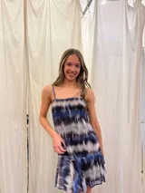 Vestido corto de tirantes finos con estampado tie-dye en tonos azul, negro y gris. Presenta un escote recto con frunce central y un volado en el ruedo de una textura diferente.