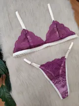 Conjunto de lencería compuesto por un bralette triangular y una bombacha tipo tanga. Ambas piezas están confeccionadas en encaje de color fucsia con detalles de terminaciones y breteles en color crema.