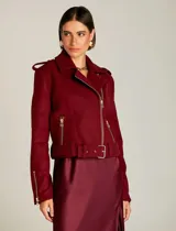 Chaqueta estilo biker de lana color bordó, con solapas amplias, cierre frontal cruzado y cremalleras metálicas doradas. Presenta hombros estructurados, cinturón ajustable en la cintura y forro interno.