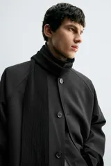 Trench de corte oversized confeccionado en tejido compacto con mezcla de lana. Presenta cuello solapa, cierre frontal con botonadura, mangas largas y bolsillos de vivo en la cadera.