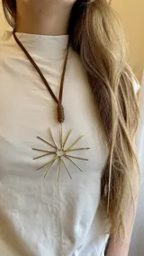 Collar con tiento de cuero marrón y dije grande de bronce con forma de estrella o sol.