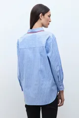 Camisa de corte clásico con estampado de rayas verticales en tonos celestes y blancos. Presenta un detalle de bordado decorativo en color rojo a lo largo de la botonadura frontal y el cuello, mangas largas con puños abotonados y un bolsillo frontal en el pecho.