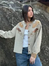 Campera color beige con apliques de cuero marrón en hombros y frente, corte recto y cierre con botones.