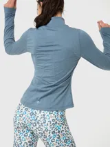 Campera deportiva de ajuste entallado, confeccionada en tejido técnico suave de color azul melange. Presenta cuello alto con cierre frontal, mangas largas con orificio para pulgar y bolsillos laterales con cierre.