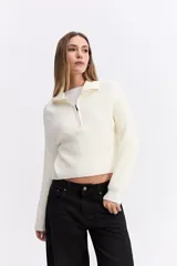 Buzo de tejido de punto con trama marcada, color blanco, con cuello alto y cierre frontal parcial. Presenta mangas largas con puños acanalados y un corte recto.