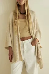 Ruana de tejido de punto color beige claro, con textura abierta y mangas anchas.