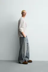 Camiseta relaxed fit color beige con cuello redondo y manga corta. Presenta un estampado frontal de un cartón de leche de fresa con una pajita, texto en japonés y la frase "SWEET MOMENTS".