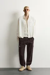 Pantalón cargo de corte ajustado en color negro, confeccionado en tejido de algodón con elasticidad. Presenta cintura elástica con cordón ajustable, bolsillos laterales tipo cargo con solapa y bajo con puños elásticos.