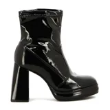 Bota corta de mujer color negro, con acabado charol brillante. Presenta un taco ancho y alto, y una plataforma delantera. El caño es ajustado, tipo calcetín, con textura elástica en el borde superior.