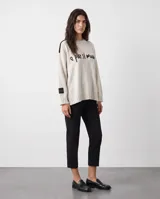 Sweater oversized crudo de tejido de punto, con hombros caídos y mangas largas. Presenta líneas negras en contraste en los hombros, bordado artesanal con la frase "e pur si muove" en el frente y aberturas laterales en el dobladillo.