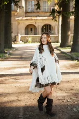 Poncho de lana merino color crudo con cuello alto, diseño amplio y flecos en el ruedo. Presenta bordados decorativos en tono chocolate y detalles de flecos en los hombros.