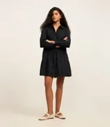 Vestido corto de corte evasé confeccionado en tricolina de algodón, color azul. Presenta cuello camisero, cierre frontal de botones y un panel central con detalle bordado calado. Posee mangas largas con puños abotonados.