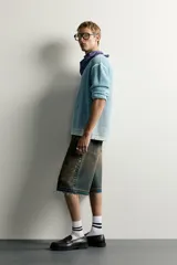 Bermuda de denim de algodón con efecto lavado desgastado en tonos marrones y azules. Tiene tiro medio, diseño de cinco bolsillos, pierna recta de corte holgado y bajo con acabado irregular. Cuenta con cierre frontal de cremallera y botón metálico.