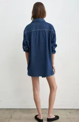Camisa de jean azul, de corte holgado y manga larga, con cuello camisero y cierre frontal de botones oscuros.