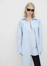 Camisa de corte oversize y diseño largo, confeccionada en algodón. Presenta cuello camisero, escote en V profundo con tiras largas integradas y mangas largas con puños abotonados.