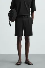 Bermuda de hombre color verde claro, de corte regular y tiro medio, con pinzas frontales, bolsillos laterales y bolsillos traseros de vivo. Cierre frontal con botón y cremallera.