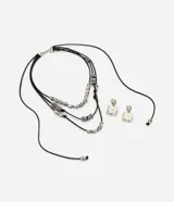 Conjunto de bijouterie compuesto por un collar multicapa de hilo encerado negro con separadores metálicos texturizados y un par de aros cuadrados con superficie texturizada.