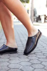 Zapatos tipo mules de cuero negro, con punta fina y detalle de charol en el borde superior.