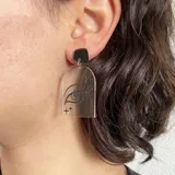 Aros colgantes con base superior negra y pieza inferior transparente con diseño de ojo grabado.