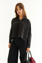 Camisa de corte oversize y estilo casual, confeccionada en algodón negro con costuras a contratono en color blanco. Presenta cuello camisero, cierre frontal parcial, mangas largas y un bordado distintivo en el puño.
