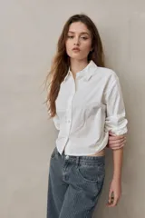 Camisa de algodón blanca de calce relajado y largo cropped, con cuello clásico, cierre frontal con botones y mangas largas.