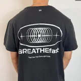 Remera negra de corte regular con estampa gráfica en la espalda que incluye un diseño circular abstracto y el texto BREATHEfast.