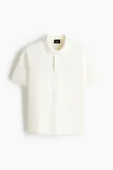 Remera polo de manga corta de H&M en punto texturizado color blanco, con cuello clásico, tapeta con botones y ribetes acanalados en puños y bajo.