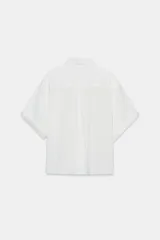 Camisa de corte fluido confeccionada en mezcla de modal, con cuello solapa, manga corta y bolsillo de plastrón en el delantero. Presenta cierre frontal con botones ocultos por tapeta y bajo con aberturas laterales.