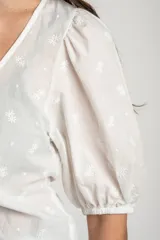 Blusa marrón de algodón con bordados sutiles, escote en V, mangas cortas abullonadas y detalle de fruncido con cordón ajustable en el centro del frente.