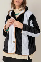 Campera de textura suave y afelpada con diseño de rayas verticales en blanco y negro. Presenta un corte recto, cuello con solapas y cierre frontal con botones. Los bordes están terminados con un ribete en color tostado que aporta contraste y estructura a la prenda.