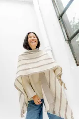 Ruana color crudo con rayas horizontales color marrón y flecos en el borde inferior.