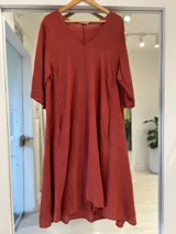 Vestido midi de lino color terracota, con escote en V, mangas tres cuartos y corte amplio y fluido con bolsillos laterales.