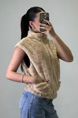 Chaleco de piel sintética color beige, con cuello alto, cierre frontal y bolsillos laterales.